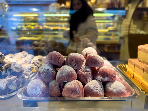 Italian food background: Light and fluffy fried balls of dough are one of Italy’s tastiest treats and one of the more traditional Roman desserts. View from a patisserie window with people reflection on glass.