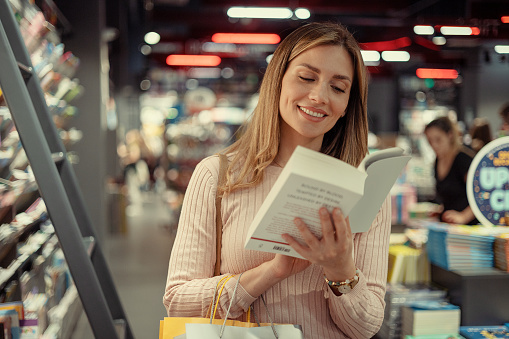 Photo of young woman reading impressum for book that she just grabbed from book shelf. Young woman is spending her free time at bookstore