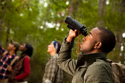 Group of friends camping and hiking using binoculars. Bird watching.