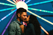Young couple kissing in front of a Ferris wheel. Girl kissing her boyfriend in an amusement park at night.