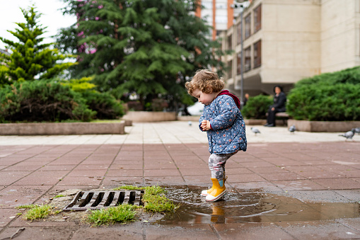 Girl in jacket and yellow rubber boots runs through the puddles.