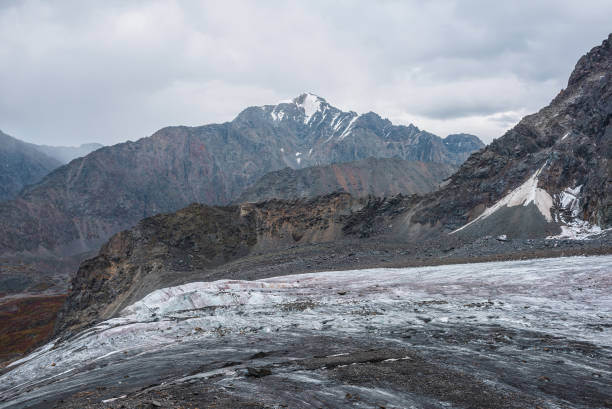 istock Awesome landscape with long glacier tongue against high mountain range with sharp rocky peaked top in overcast weather. Cone shaped pointy peak in dramatic cloudy sky. Large glacier among sharp rocks. 1493623949