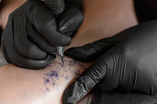 Tattoo master protective gloves make a tattoo in black ink on the hand of the girl. Close-up.