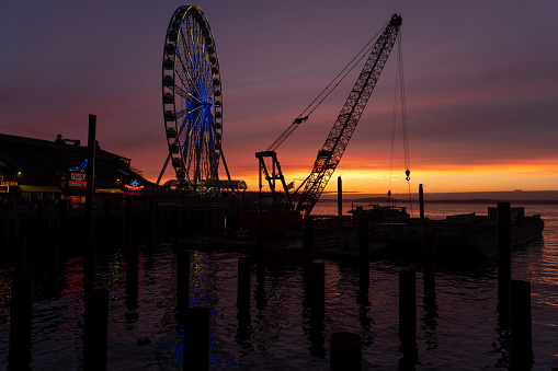 Seattle, USA - Feb 12th, 2023: A vivid sunset over Elliott Bay with The Great Seattle Wheel and new pier construction the waterfront.