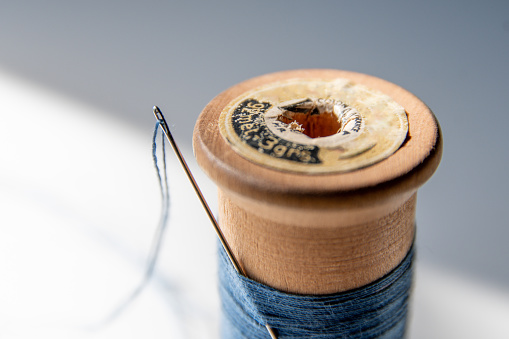 Antique blue sewing thread spool and threaded needle. Without people. Macro photography.