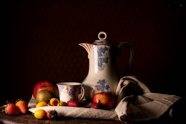 Still life front photograph with fruit and antique chocolate jug and cup. Plain black background, wooden base. Without people.