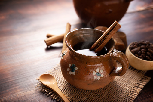 Authentic homemade mexican coffee (cafe de olla) served in traditional handmade clay mug (Jarrito de barro) on rustic wooden table.