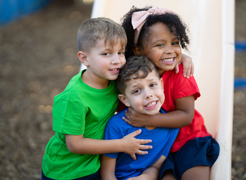 Three preschool children are having fun playing on the playground of their daycare