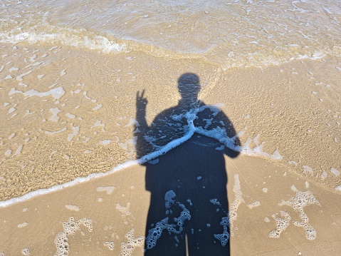 The shadow of a man on the sand during the high tide of the sea wave.