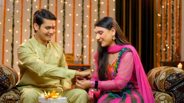 Cheerful sister tying rakhi on her brother's wrist on the occasion of Raksha Bandhan - festive feel, brother sister relationship