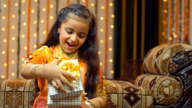 Young girl with a present in traditional wear on Raksha Bandhan or Bhai Dooj - the festive season, Indian Model Cute little sister opening a gift box from her younger brother on the occasion of Rakhi/Tika - Surprise gift bhai tika stock pictures, royalty-free photos & images