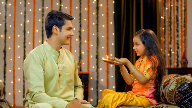 Young Indian siblings happily performing Raksha Bandhan Or Bhai Dooj traditions - Indian Model Cute little sister celebrating Raksha Bandhan / Bhai Dooj rituals of doing aarti / pooja of her handsome elder brother- festive season bhai tika stock pictures, royalty-free photos & images