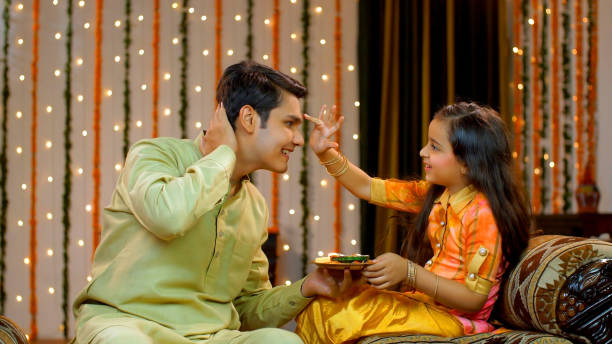 Young siblings celebrating Raksha Bandhan or Bhai Dooj festival together - Happy family , Indian Model Pretty sister happily putting tika on her elder brother's forehead in traditional wear on the occasion of rakhi / tika bhai tika stock pictures, royalty-free photos & images