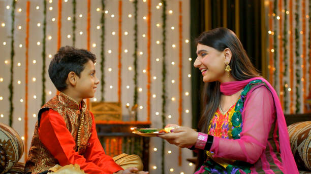 Young Indians happily performing Raksha Bandhan on Bhai Dooj traditions - Indian Model Pretty elder sister celebrating Raksha Bandhan / Bhai Dooj rituals of doing aarti / pooja of her sweet little brother bhai tika stock pictures, royalty-free photos & images
