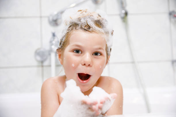 nettes kind mit shampoo-schaum und blasen auf dem haar beim baden. porträt eines glücklich lächelnden vorschulmädchens gesundheits- und hygienekonzept. wäscht die haare selbst. - romrodinka stock-fotos und bilder