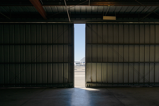 From within the hangar, a glimpse of the outside world is visible through the narrow opening of the doorway, revealing several aircraft and a slice of the sky.