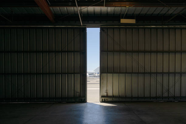 Inside the hanger From within the hangar, a glimpse of the outside world is visible through the narrow opening of the doorway, revealing several aircraft and a slice of the sky. airplane hangar stock pictures, royalty-free photos & images