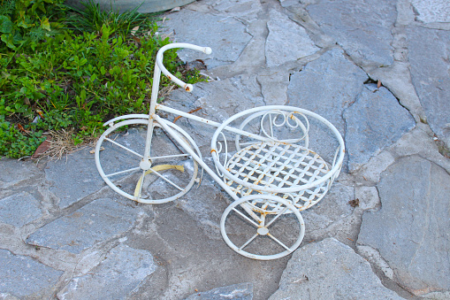 A small white bicycle that serves as a pot holder on a stone surface
