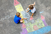 Two little kids boys drawing knight castle with colorful chalks on asphalt. Happy siblings and friends having fun with creating chalk picture and painting. Creative leisure for children in summer.
