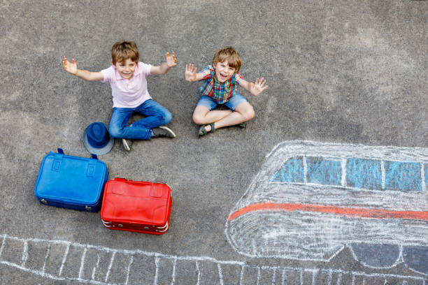 zwei kleine kids jungs haben spaß mit bahn-bild-zeichnung mit bunten kreiden auf asphalt. kinder, die spaß an kreide und kreidefalerei haben. urlaub und reisen. freunde mit koffern - romrodinka stock-fotos und bilder