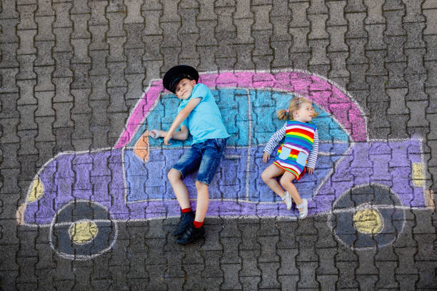 zwei kleine kinder, kind junge und kleinkind mädchen spaß mit auto bild zeichnung mit bunten kreide auf asphalt. geschwister malen auf dem boden und spielen zusammen. kreative freizeit für kinder - romrodinka stock-fotos und bilder