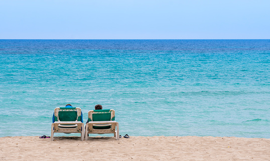 Rear view of two people laying on sun lounger on the beach against sea, Mallorca Cala Millor