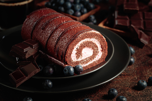 Chocolate roll cake with blueberries and a broken black chocolate bar.