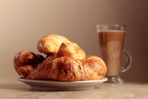 Freshly baked croissants and coffee with cream on a beige ceramic table.