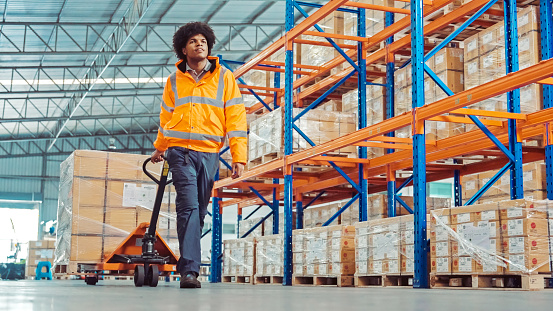 an African American warehouse worker moving a pallets jack in the factory warehouse