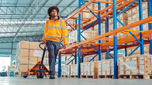 an African American warehouse worker moving a pallets jack in the factory warehouse stock photo