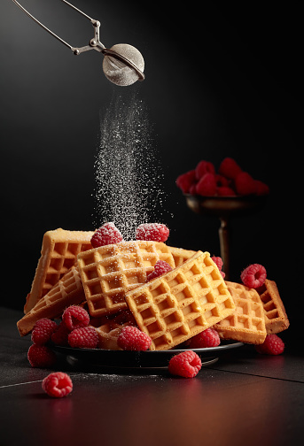 Belgian waffles with raspberries sprinkled with powdered sugar. Waffles with raspberries on a black background.