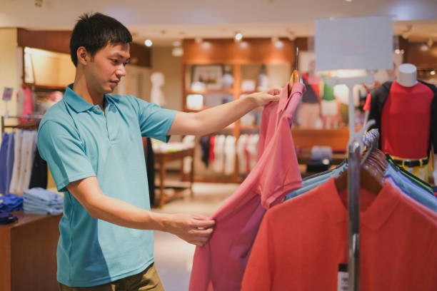 junger asiatischer mann kauft im bekleidungsgeschäft ein - polo shirt multi colored clothing variation stock-fotos und bilder