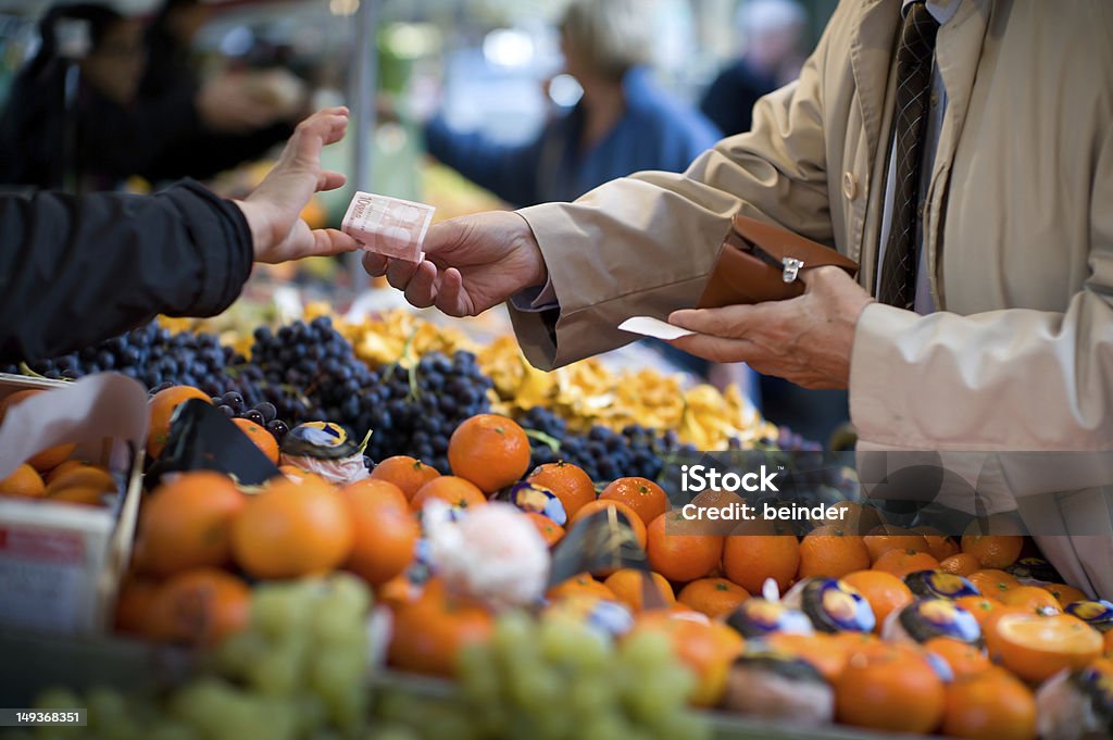 Vendor accepts payment at a street market A man reaches across a row of fruit in an outdoor market to pay a vendor with a 10 Euro bill. Focus is tight on the bill changing changing hands. The foreground and background are out of focus. Food Stock Photo