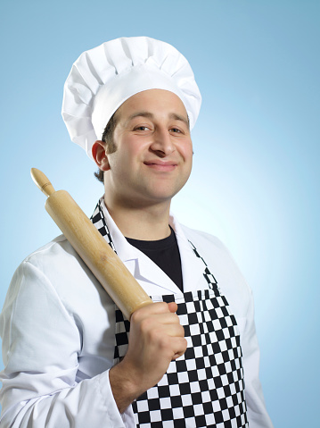 Chef in uniform holding a rolling pin looking at camera