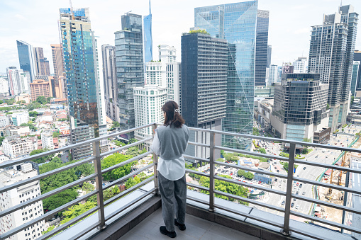 An Asian business woman using smart phone on rooftop at downtown skyscraper