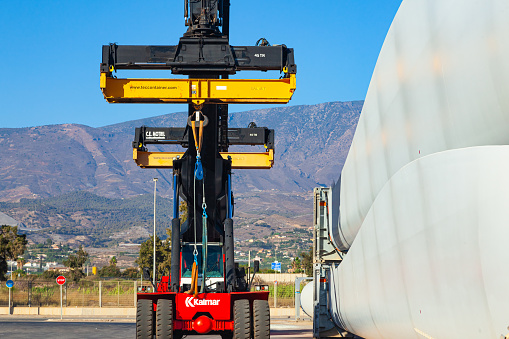 Motril, Spain - 09.27.2022: A four-wheeled mobile container loaders parked at the seaport, next to the storage blades for wind turbines.