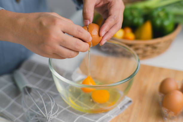 jeune femme cuisinant dans une cuisine lumineuse, des jaunes d’œufs frais concassés faits à la main dégoulinant dans le bol. préparer des ingrédients pour une cuisine saine. nourriture faite maison - break eggs domestic kitchen breaking photos et images de collection