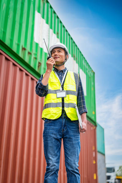 An Asian male management and transportation control engineer stood in front of the container and communicated with each other through a walkie talkie. stock photo