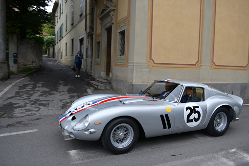 Cernobbio, Como - May 21, 2023: Concorso d'Eleganza Villa d'Este 2023.\nThe Ferrari 250 GTO is a GT car produced by Ferrari from 1962 to 1964 for homologation into the FIA's Group 3 Grand Touring Car category. It was powered by Ferrari's Tipo 168/62 Colombo V12 engine. \n\nIn Europe, the Concorso d'Eleganza Villa d'Este has developed into a meeting point for lovers of high-quality classic automobiles.\nActive automotive designers are also looking for inspiration for their work there.\nIn addition, the event is given a special touch by the Villa d'Este, a former cardinal's palace with park, located directly on the lake\na neat setting and a social touch.\nOn Sunday, vehicles for the general public will be shown on the grounds of the neighboring Villa Erba.\nThe vehicles drive early in the morning from Villa d'Este to Villa Erba through the small town of Cernobbio\nat Como\non the public road, on Via Regina\n\nIn the background you can see the church Chiesa di Maria delle Grazie.\n\n\n\nThe event traditionally takes place on the third weekend in May each year.\n\nA jury decides on the two prizes \