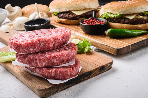 Raw ground beef meat cutlets for burger on white textured background.