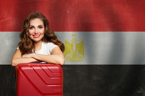Welcome to Egypt. Cheerful woman with red suitcase on Egyptian flag background. Travel, work, education and internship in Egypt