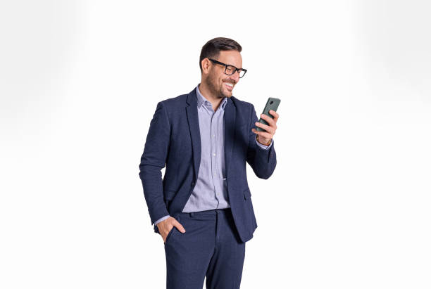 hübscher männlicher professioneller manager mit hand-in-pocket-nachrichten online auf dem handy. eleganter geschäftsmann, der e-mails auf dem handy liest, während er isoliert vor weißem hintergrund steht - isolated cheerful businessman smiling stock-fotos und bilder