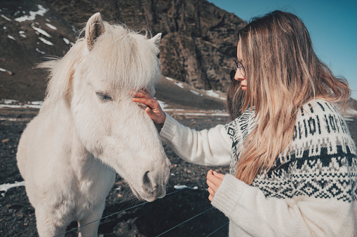 A female animal lover strokes a horse's head while standing surrounded by wild nature