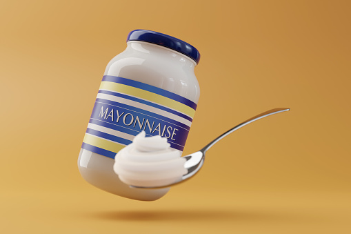 Glass bottle jar of mayonnaise has a spoonful of out-focus mayo as foreground and a plain yellow background. Illustration of the concept of creamy sauce