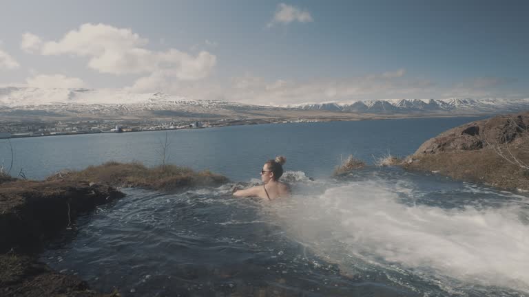 Relaxed female tourist enjoys swimming in an outdoor hot spring. Iceland