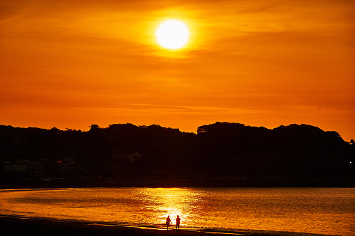 Children standing on beach at sunset.