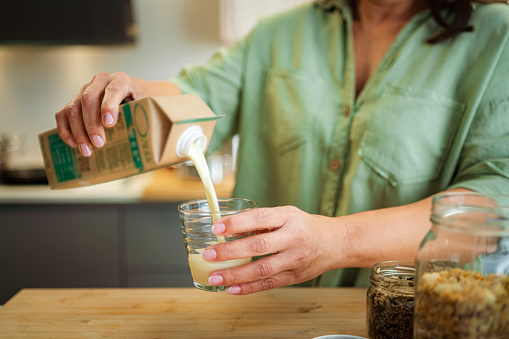 Cropped shot of woman's hands pouring milk from a carton package into a glass for healthy meal