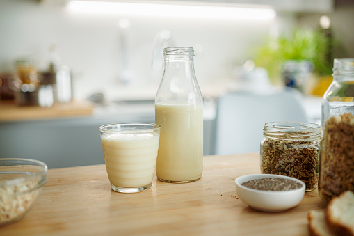 Glass and bottle of vegan milk shot on kitchen counter. Soy milk, oat milk, almond milk.