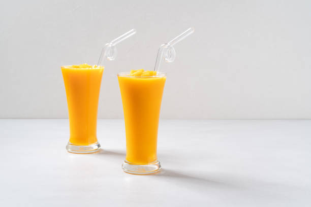 Fresh beautiful delicious mango juice. Close up design concept of smoothie cold drink in glass cup with glass straw on gray table background.