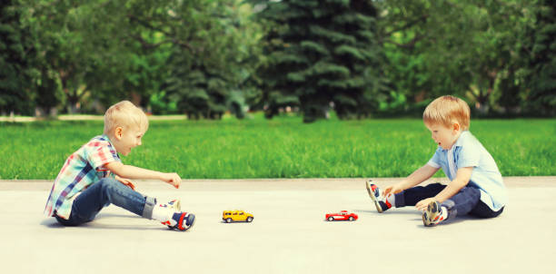 Two boys children playing together with toys cars in the park on summer day stock photo